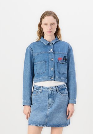 Veste en denim courte bleu clair avec deux poches avant, boutons en argent et patches brodés. Associée à une jupe en denim assortie.