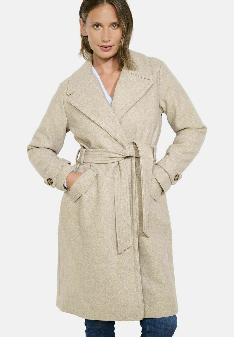 Smėlio spalvos vilnos mišinio paltas su diržu, plačiais atvartais ir šoninėmis kišenėmis. Papuoštas mygtukais ant rankovių ir pritaikytas fasonas.