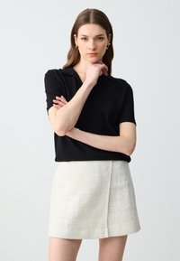 Polo noir à manches courtes, en tissu tricoté doux, associé à une jupe texturée de couleur crème avec une fente sur le devant.