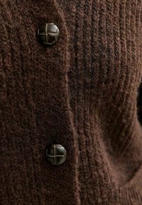 Tessuto lavorato a maglia marrone con due bottoni rotondi di un marrone scuro, decorati con un motivo intrecciato, fissati verticalmente su un indumento.