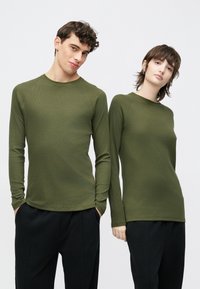 Oliivrohelised pikkade varrukatega ülaosad ümmarguse kaelusega, millel on soonikuline tekstuur ja kitsas lõige, kombineeritud mustade lõdva lõikega pükstega.