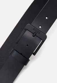 Ceinture en cuir noir avec une finition mate, dotée d'une boucle rectangulaire avec le logo "BOSS" en relief et plusieurs trous d'ajustement.