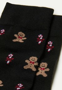 Sorte strikkede sokker med et mønster af peberkager og slikstokke i tan, rød og hvid. Blød tekstur med en behagelig ribbet manchet.