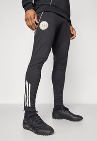 Pantalones deportivos negros con un diseño ajustado, que presentan un logo circular en el muslo y franjas blancas a lo largo del costado. Hechos de una tela suave.