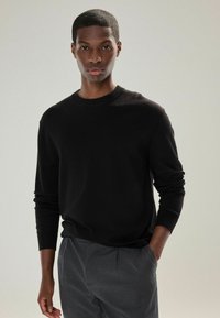 Black sweater with long sleeves and crew neckline, made from a smooth material. Paired with gray trousers, minimalistic design.