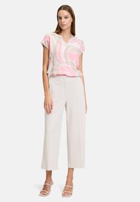 Lekka bluzka z krótkim rękawem w różowo-beżowym kwiatowym wzorze, połączona z kremowymi spodniami typu wide-leg i beżowymi sandałami na paski.