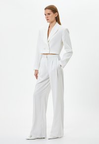 Weißes Cropped-Blazer mit zwei Knöpfen, kombiniert mit hoch taillierten, weit geschnittenen Hosen. Glatter Stoff, taillierte Passform, minimalistisches Design.