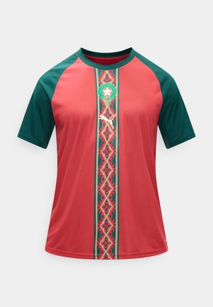 Piros és zöld rövid ujjú sportruházat mintás függőleges csíkkal, Puma logóval és fociemblémával a gallér közelében.