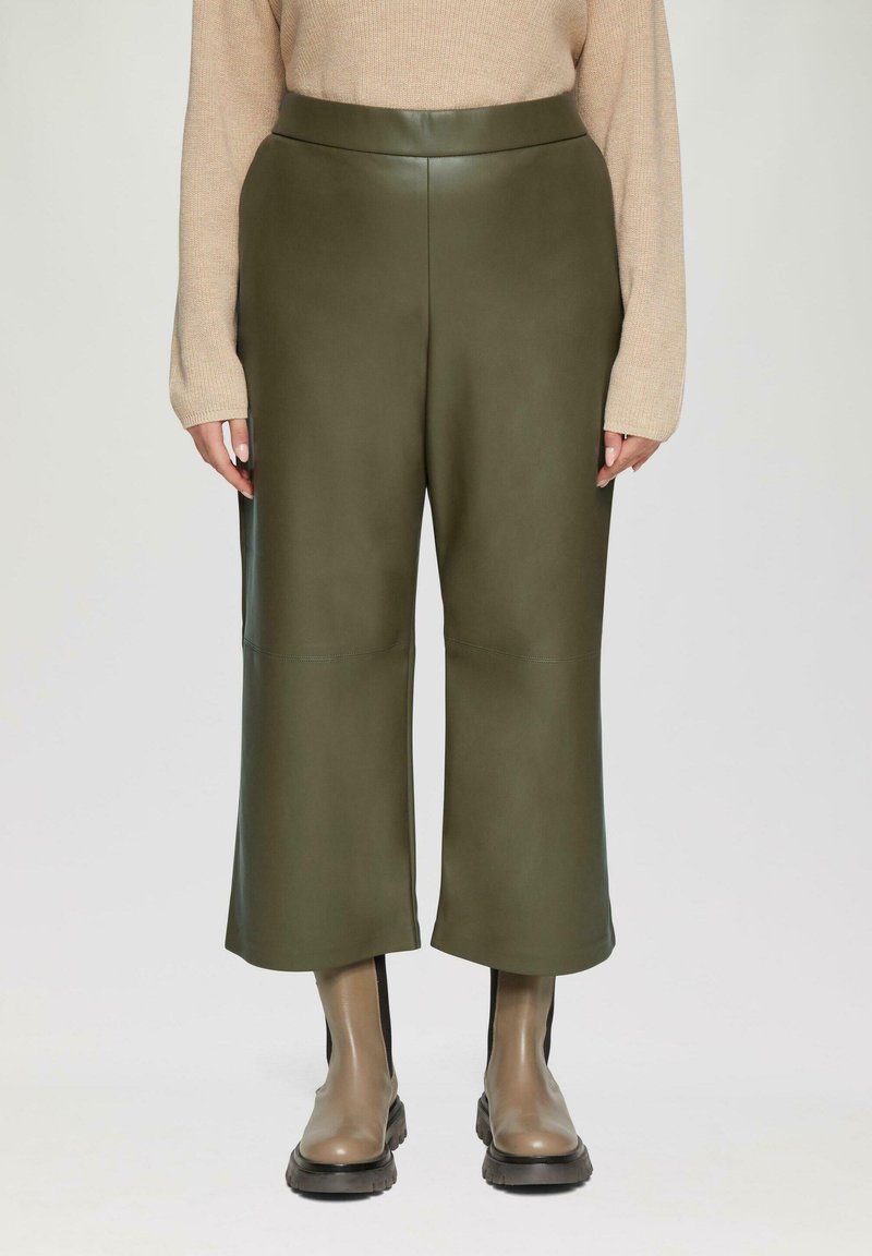 Groene faux leren wijde broek met een gladde textuur en hoge tailleband; gecombineerd met bruine enkellaarsjes.