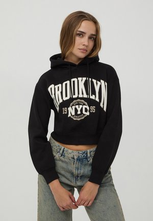 Felpa corta nera con testo bianco "BROOKLYN NYC 1995"; materiale in cotone; presenta una tasca frontale e cappuccio con cordini; vestibilità rilassata.