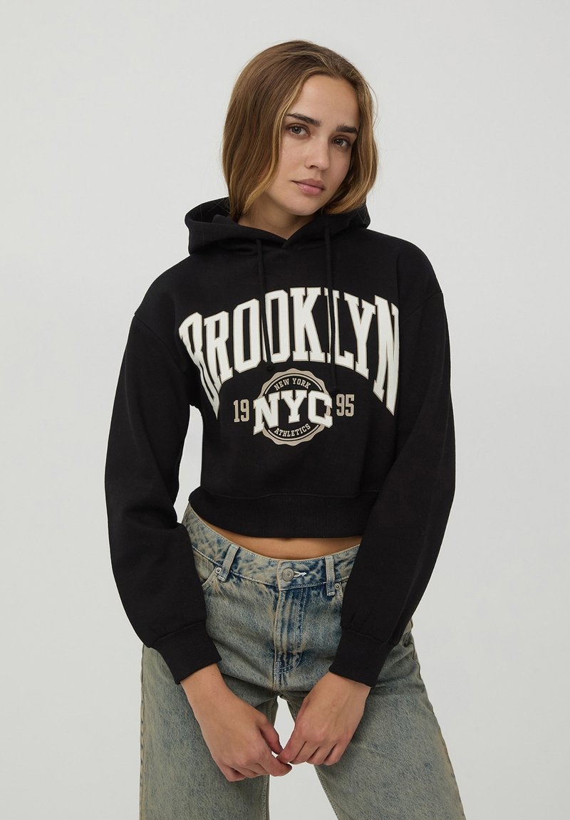 Felpa corta nera con testo bianco "BROOKLYN NYC 1995"; materiale in cotone; presenta una tasca frontale e cappuccio con cordini; vestibilità rilassata.