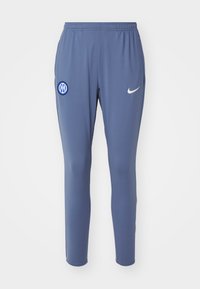 Blauwe sportbroek met een elastische tailleband, met een wit Nike-logo en een cirkelvormig blauw logo op de linkerdij. Glad stoftextuur.