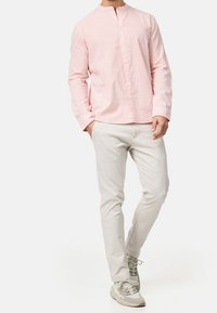 Maglietta a maniche lunghe a righe rosa e bianche con collo alla coreana, bottoni sul davanti, abbinata a pantaloni chiari e sneaker grigie.