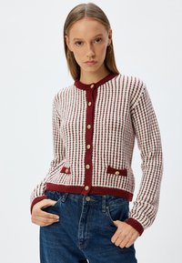 Sweter z dzianiny w czerwono-białe paski, okrągły dekolt, złote guziki i dwie przednie kieszenie. Miękka, teksturowana tkanina.