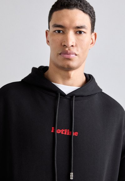 Črna kapuca iz bombaža, ki ima sprednji žep ter rdeče vezene besede "hotline." Zategovalne vrvice z kovinskimi detajli.