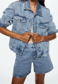 Jasnoniebieska dżinsowa kurtka z klasycznym kołnierzykiem, przednimi kieszeniami i zapięciem na guziki, połączona z dopasowanymi szortami dżinsowymi z wysokim stanem.
