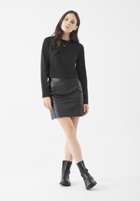 Top negro de manga larga y una falda lápiz de cuero negro. El conjunto se complementa con botas de tobillo negras, con suela gruesa y acabado texturizado.