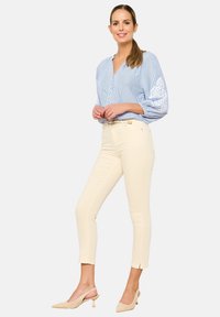 Blusa de botones azul claro a rayas con mangas abullonadas, pantalones beige ajustados y zapatos de tacón color beige. El conjunto presenta detalles sutiles.