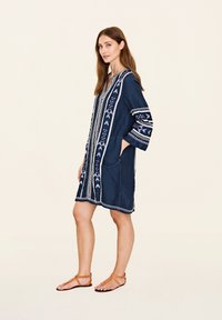 Tunică bleumarin cu modele brodate albe, cu decolteu în V, mâneci trei sferturi, două buzunare frontale și croi lejer.