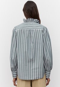 Camicia a righe grigio chiaro-blu con righe verticali bianche, colletto alto e dettagli plissettati nella parte posteriore. Maniche lunghe con polsi abbottonati.