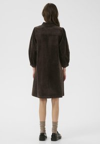 Brown corduroy dress with a collar, puffed sleeves, and a straight cut to the knee. Worn with ribbed cream socks and black shoes.