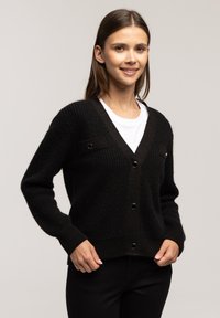 Czarny sweter z dzianiny z dekoltem w serek, długimi rękawami, dwiema przednimi kieszeniami z akcentami oraz zapięciem na guziki. Teksturowana tkanina z prążkowanymi mankietami.