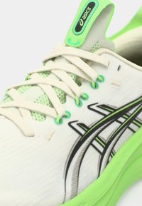 Chaussure de sport blanche avec des accents verts, dotée d'une tige respirante, d'un design distinctif à rayures noires et d'une semelle intermédiaire texturée.