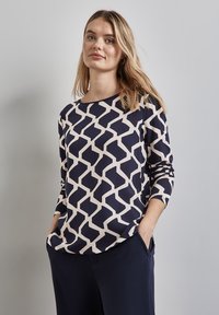 Granatowy top z długim rękawem z kremowym geometrycznym wzorem, okrągłym dekoltem, luźnym krojem i miękką fakturą materiału. Idealny na codzienne wyjścia.