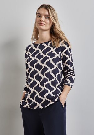 Haut à manches longues navy avec un motif géométrique crème, encolure ronde, coupe décontractée et tissu texturé doux. Convient pour une tenue décontractée.