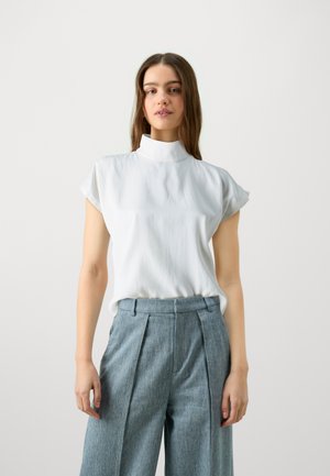 Blusa bianca a maniche corte con colletto alto, realizzata in tessuto liscio. Abbinata a pantaloni a vita alta a righe blu con pieghe.