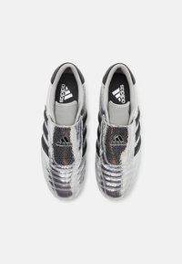 Hopeiset teksturoituneet lenkkarit mustilla raidoilla, joissa on tyylikäs muotoilu ja näkyvä logo kielen kohdalla. Pehmeä harmaa sisustus.