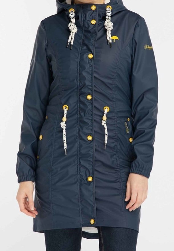 Parka imperméable bleue marine avec une silhouette ajustée, quincaillerie dorée, capuche réglable et cordons de serrage. Tissu texturé avec des poignets élastiques.