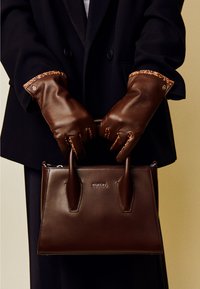 Brown leather handbag with structured shape and dual handles, featuring a smooth texture and "ROECKL" logo. Paired with brown leather gloves.