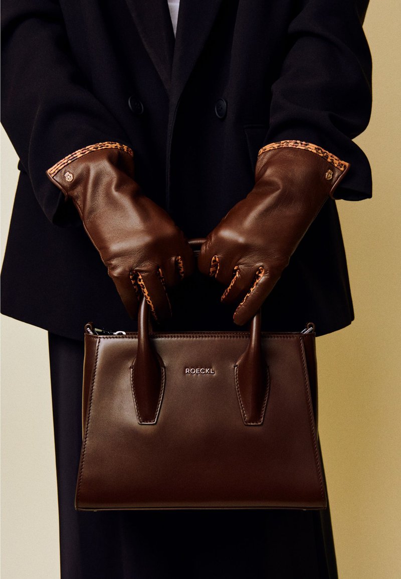 Brown leather handbag with structured shape and dual handles, featuring a smooth texture and "ROECKL" logo. Paired with brown leather gloves.