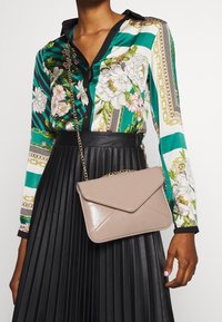 Beige obálková taška z umělé kůže s řetízkem. Disponuje diagonálním švem a hladkým, lesklým povrchem.