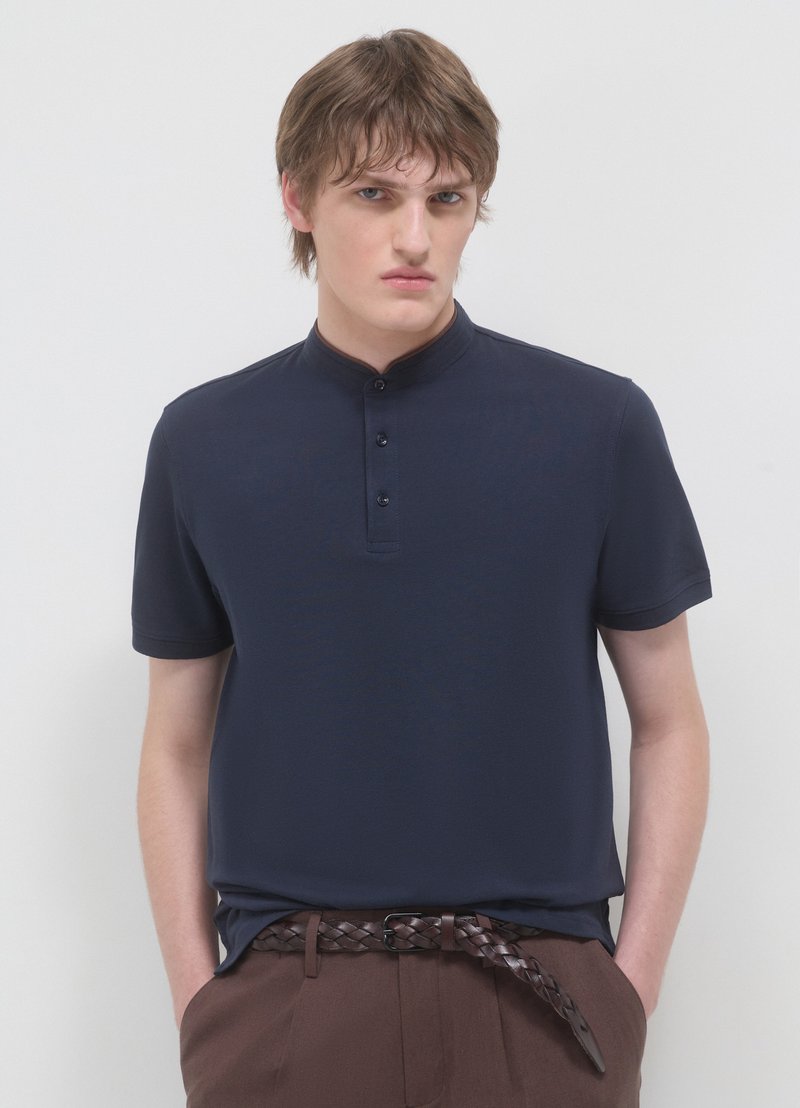 Polo blu navy con maniche corte e colletto alla coreana. Presenta tre bottoni nascosti e una texture liscia e leggera.