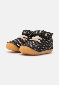 Chaussures noires avec un motif d'étoiles, en matériau texturé, lacets beiges et semelle en caoutchouc. Dispose d'une sangle ajustable avec une fermeture à pression.