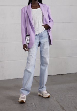 Blazer oversize lavanda, camicia bianca con texture, jeans dritti blu chiaro e sneakers beige con accenti viola. Borsa a tracolla argentata.