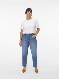 Bílá tričko s krátkým rukávem spárované se světle modrými džíny s vysokým pasem. Modelka má na sobě olivově zelené špičaté baleríny a jednoduché šperky.