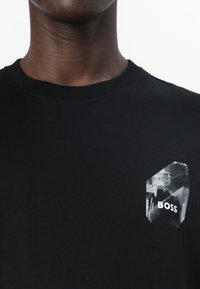 Black cotton T-shirt with a round neckline and a graphic print on the left chest featuring the word "BOSS" in white.