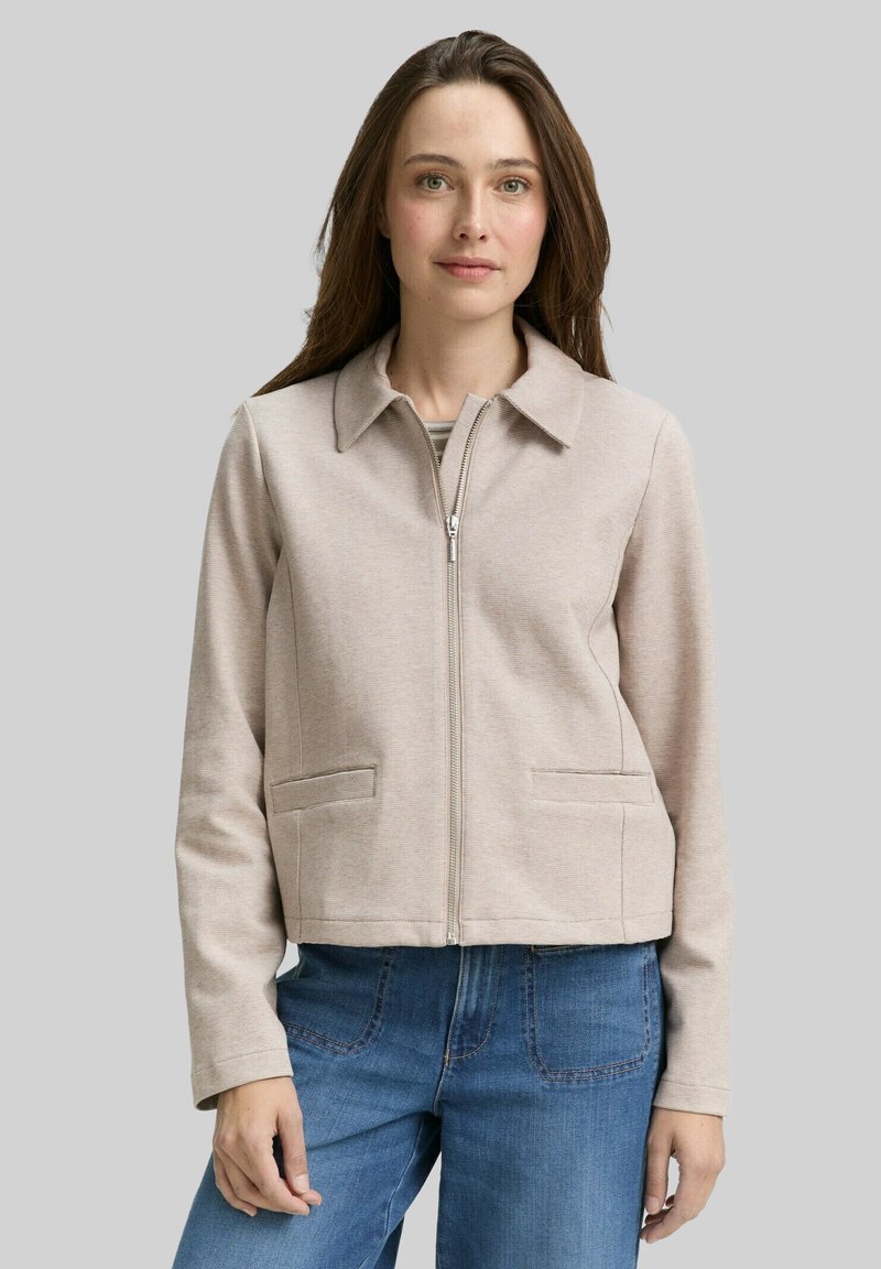 Beige cropped jasje met een kraag, rits aan de voorkant en twee zijzakken. Gemaakt van zachte stof met een gladde textuur.