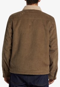Chaqueta de pana marrón con un cuello beige peludo, con un corte holgado y textura forrada. La parte trasera presenta un detalle de canalé vertical.