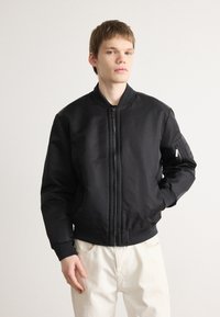 Schwarze Bomberjacke mit Reißverschluss vorne, gerippten Bündchen und Saum, ausgestattet mit einer seitlichen Tasche mit Reißverschluss und einer glatten, matten Textur.