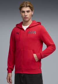 Κόκκινο hoodie με φερμουάρ, κατασκευασμένο από μείγμα βαμβακιού. Διαθέτει τσέπες τύπου καγκουρό, κεντημένο λογότυπο "AGM" και λογότυπο Puma στο στήθος. Απλός σχεδιασμός με ριμπ μανσέτες.