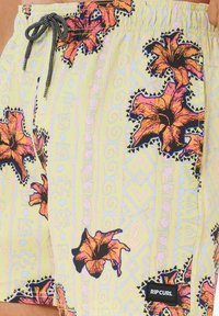 Pantaloni da bagno in tessuto giallo chiaro con un motivo floreale che presenta fiori rosa e neri. Include un cordino nero e un'etichetta con il logo.