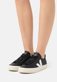 Sneaker in pelle nera con logo a contrasto bianco, superficie testurizzata, punta rotonda e suola in gomma bianca a contrasto, dotati di lacci neri.