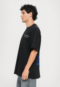 Svart oversized t-skjorte med hvite og blå grafikker. Korte ermer og rund hals. Laget av bomull, med et merke på siden.