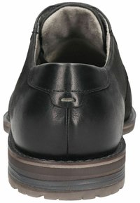 Zapato de cuero negro con tacón redondeado, textura suave y suela de goma gris. Presenta una costura en la parte trasera y un forro interior suave.