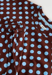 Tissu marron à pois bleu clair sur un haut à manches longues et un pantalon assorti à taille élastique avec cordon de serrage.