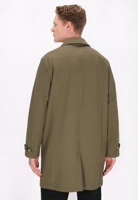 Oliven grøn trenchcoat med en glat overflade, en enkeltstående design og knapmanchetter. Bagsiden har en slids for nem bevægelse.